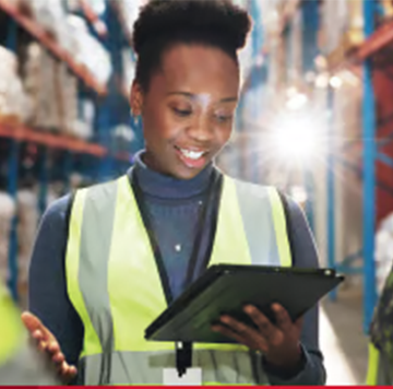 Smiling woman in a safety vest uses a tablet in an Africa-based warehouse with shelves in the background.