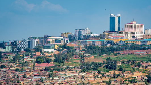 A cityscape in Africa with modern buildings rising behind a foreground of smaller homes and greenery under a blue sky.