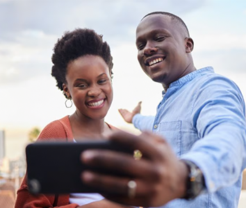 Two people in Africa smiling and taking a selfie together outdoors on a bright, sunny day.