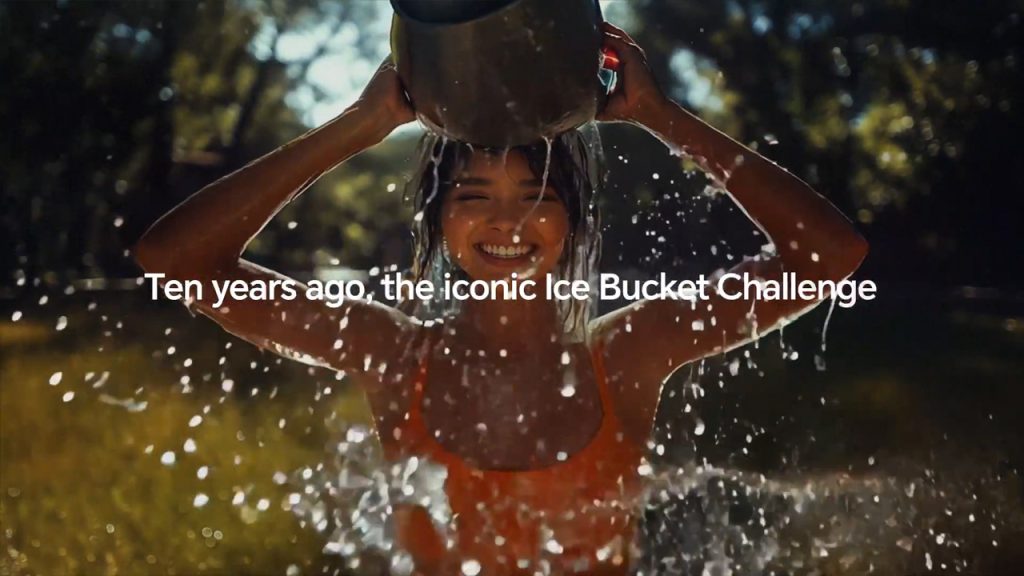A smiling young woman in an orange tank top pours a bucket of water over her head outdoors, water splashing everywhere. Sunlight filters through trees in the background. White text in the center reads, "Ten years ago, the iconic Ice Bucket Challenge.