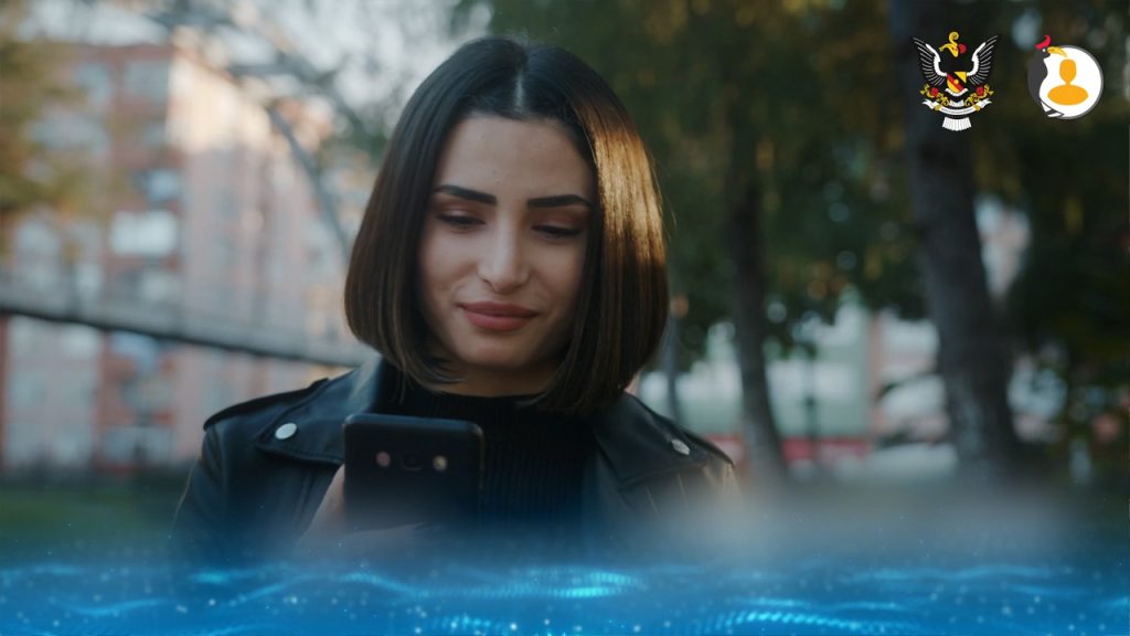 A woman with straight, shoulder-length dark hair and a black jacket looks at her phone outdoors. The background is blurred with trees and buildings. Two logos are at the top right, and a blue digital wave effect is at the bottom of the image.