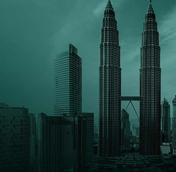 Tall twin skyscrapers with a skybridge, surrounded by other buildings under a teal-colored sky in the heart of the Asia Pacific region.