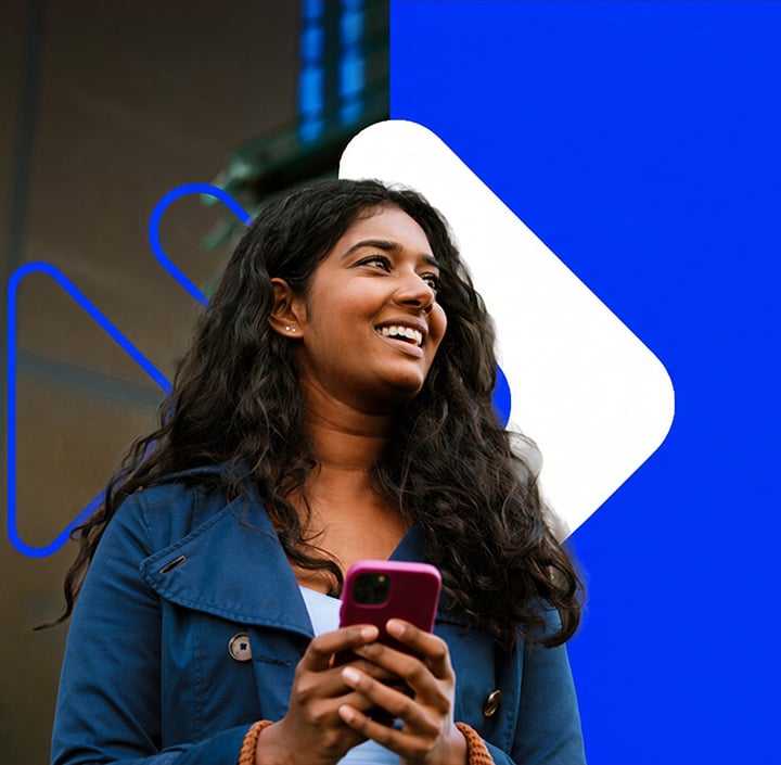 A smiling woman with long, curly dark hair holds a pink phone. She wears a blue jacket and stands in front of a split background: one side brown with blue accents, the other solid bright blue with a white geometric shape, evoking contemporary styles popular across the Asia Pacific region.