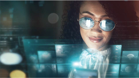 A woman with curly hair and reflective glasses looks at her smartphone, smiling. Digital interface graphics, including icons and screens, are overlaid in front of her, suggesting technology and connectivity in a futuristic setting.