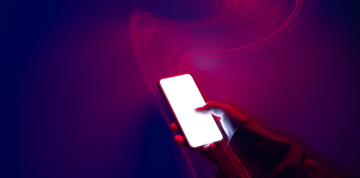 A hand holds a mobile phone with a glowing white screen against a dark blue and purple background. Pink and red light streaks curve around the phone, creating a dramatic, futuristic effect with vivid lighting contrasts.