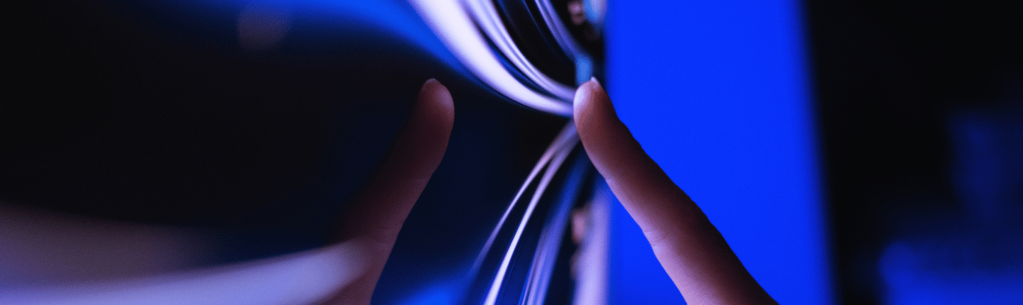 Primer plano de los dedos de una persona tocando una pantalla electrónica elegante y curva que emite una luz azul. Los dedos presionan contra la superficie lisa, lo que provoca reflejos y ligeras distorsiones en la pantalla. El fondo es un degradado de tonos azul oscuro y claro.
