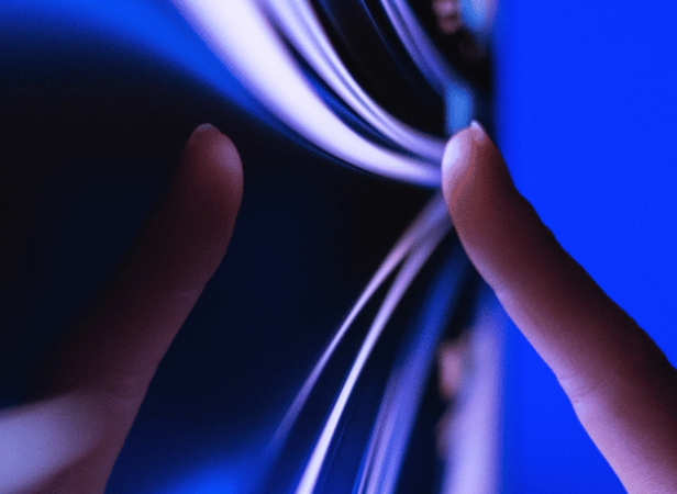Two fingers gently touch a flexible, glossy screen, which curves and ripples at the contact points. The background glows with blue and purple hues, highlighting the interaction between the hands and the modern, bendable display surface.