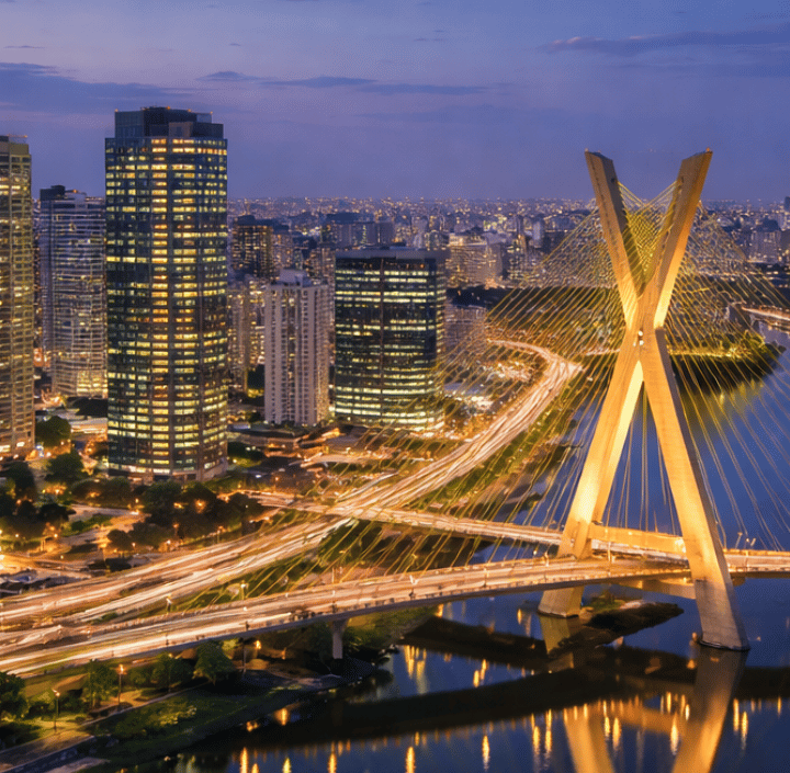 Puente atirantado con rascacielos al atardecer, luces reflejándose en el río.