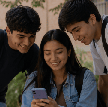 Tres estudiantes sonrientes miran juntos un smartphone al aire libre, parecen felices y comprometidos.