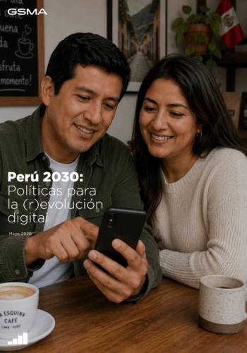 A smiling couple sits at a table, looking at a smartphone together, with coffee mugs in front of them.