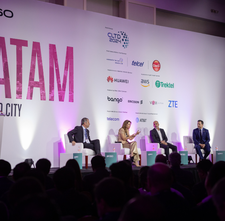 A panel of four professionals sits on a stage, engaged in a discussion at a technology conference. The backdrop features logos from various tech companies, including Huawei, AWS, and ZTE. The audience is dimly lit in the foreground, highlighting the panelists under bright stage lighting.