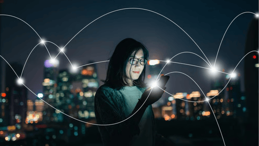 A woman using a mobile phone at night with digital connection lines, city lights blurred in the background, reflecting the dynamic networking fostered by the GSMA regional interest group.