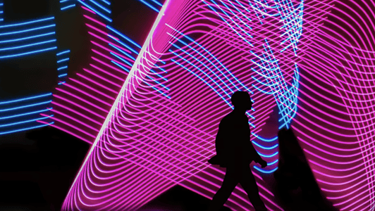 Silhouette of a person walking in front of vibrant pink and blue neon light patterns, capturing the dynamic energy often seen at GSMA regional interest group events.