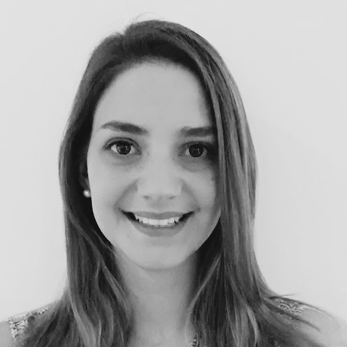 Black and white portrait of a smiling woman with long, straight hair. She is wearing a sleeveless top and pearl earrings. The background is a plain, light color. Her expression is friendly and welcoming.