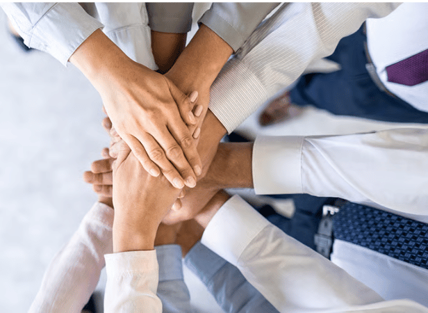 A group of people stacking their hands together in a show of teamwork and unity, demonstrating the collaborative spirit found in AA.35.