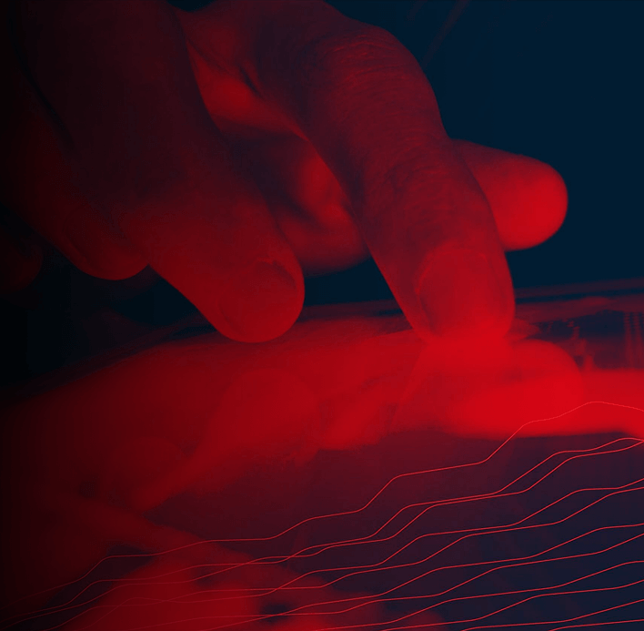 A close-up of fingers touching a tablet or touchscreen, illuminated by a red light. Curved, glowing red lines appear across the bottom, suggesting digital or technological interaction in a dark setting.