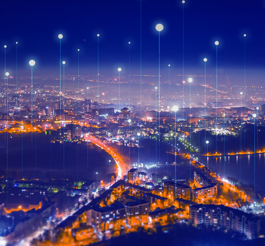 A nighttime cityscape with glowing dots connected by light lines above the buildings, symbolising digital connectivity. The city is illuminated by streetlights and building lights, with a bright, winding road visible in the foreground—evoking the seamless flow of 6 GHz mobile networks weaving through urban life.