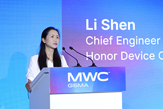 A woman with long dark hair speaks at a lectern labelled “MWC GSMA” in front of a blue screen displaying the name “Li Shen, Chief Engineer, Honour Device Co.” Two microphones are on the lectern.