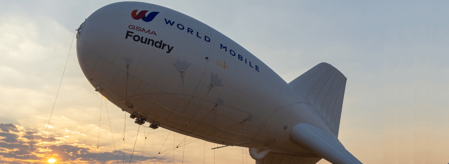 Airship with "world mobile" branding flying at sunset.