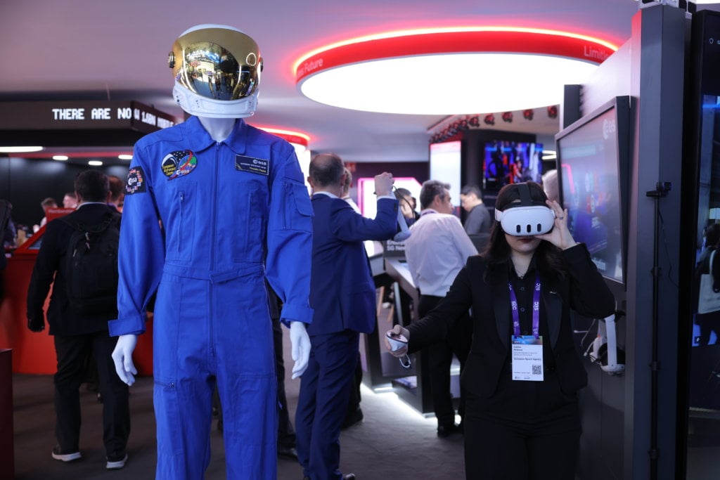 A person in business attire uses a vr headset at an event next to a mannequin dressed in an astronaut suit.