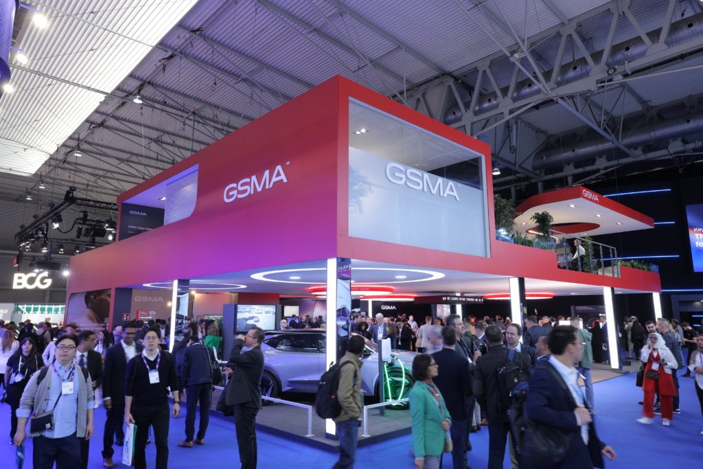 Corporate exhibition booth at a trade show with attendees walking by.