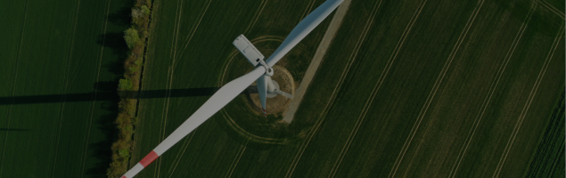 Aerial view of a wind turbine in a green field casting a long shadow.