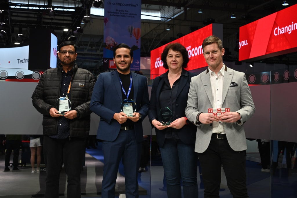 Four individuals posing with awards at an event.