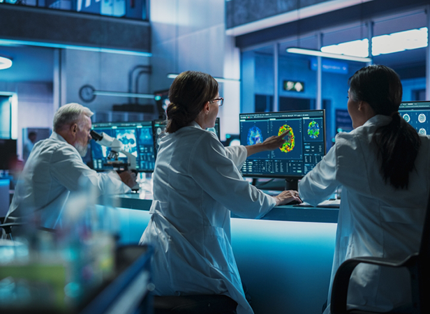 A group of scientists in a modern lab, wearing white lab coats, analyze brain scans on computer monitors. A female scientist points at a colorful brain scan. The lab is equipped with advanced technology and illuminated by cool blue lighting, creating a focused atmosphere.