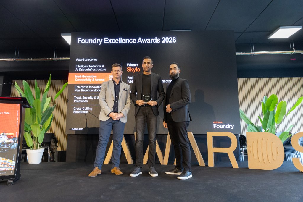 Three men in suits stand on stage holding an award, with a display reading "Foundry Excellence Awards 2026.