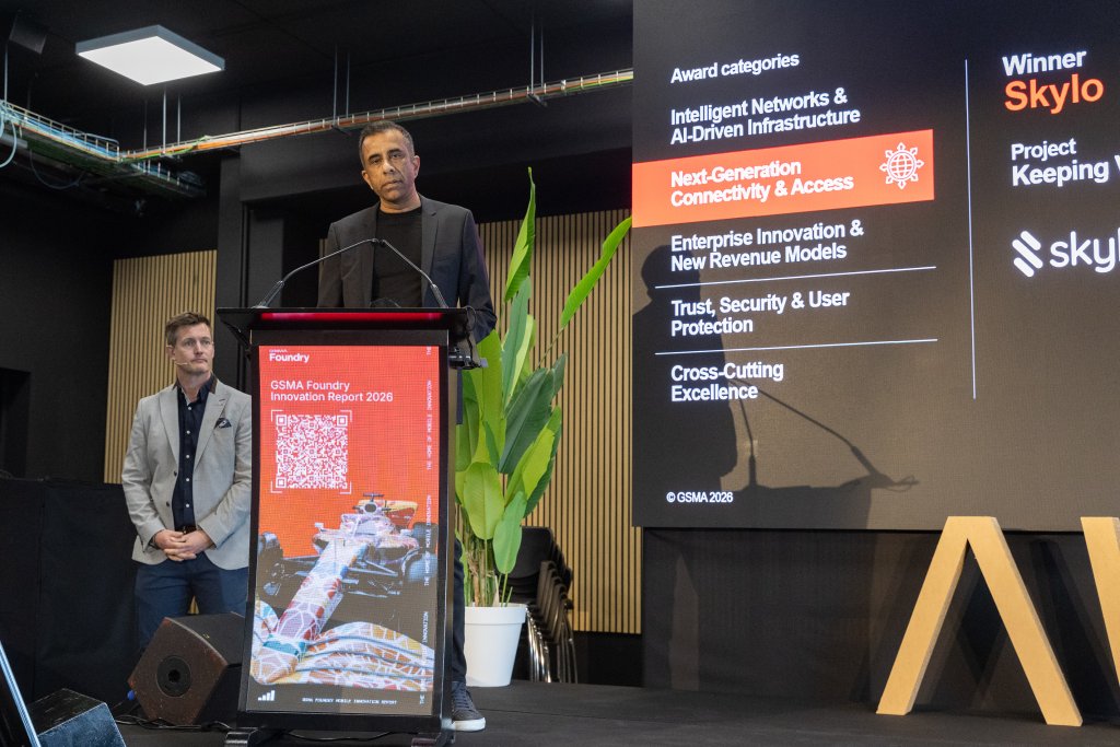 Two men stand on stage at an awards event, with a screen displaying "Next-Generation Connectivity & Access.