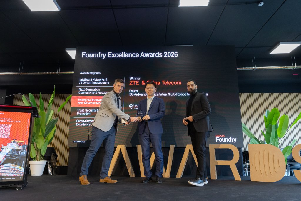 Three men on stage at the Foundry Excellence Awards 2026, holding a trophy in front of a presentation screen.