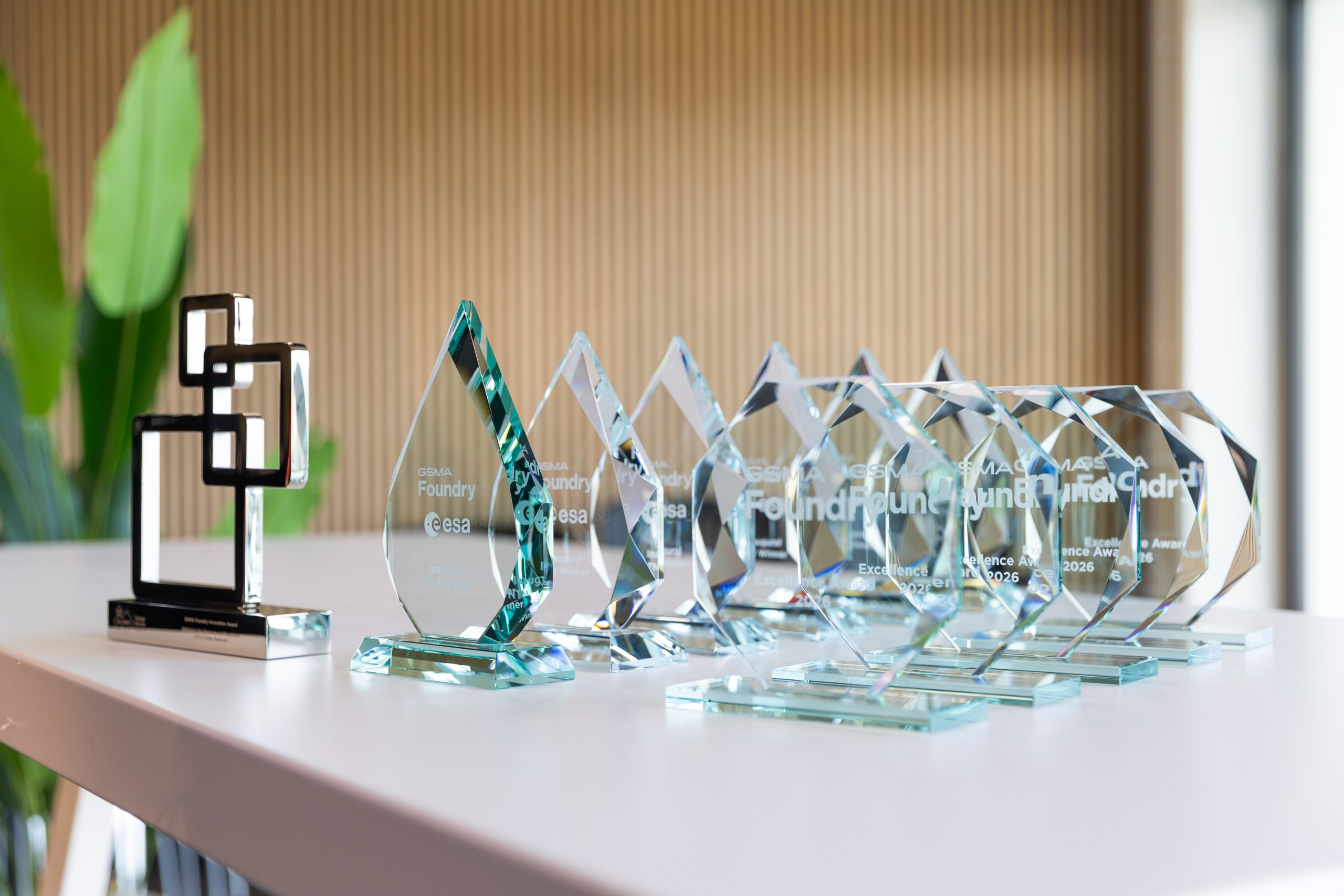 Several glass awards and one black metal award are displayed on a white table in a modern setting.
