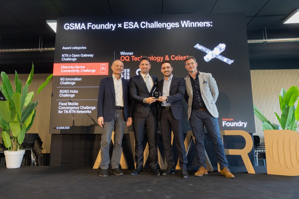 Four men in suits hold a trophy on stage in front of a GSMA Foundry x ESA Challenges Winners screen.