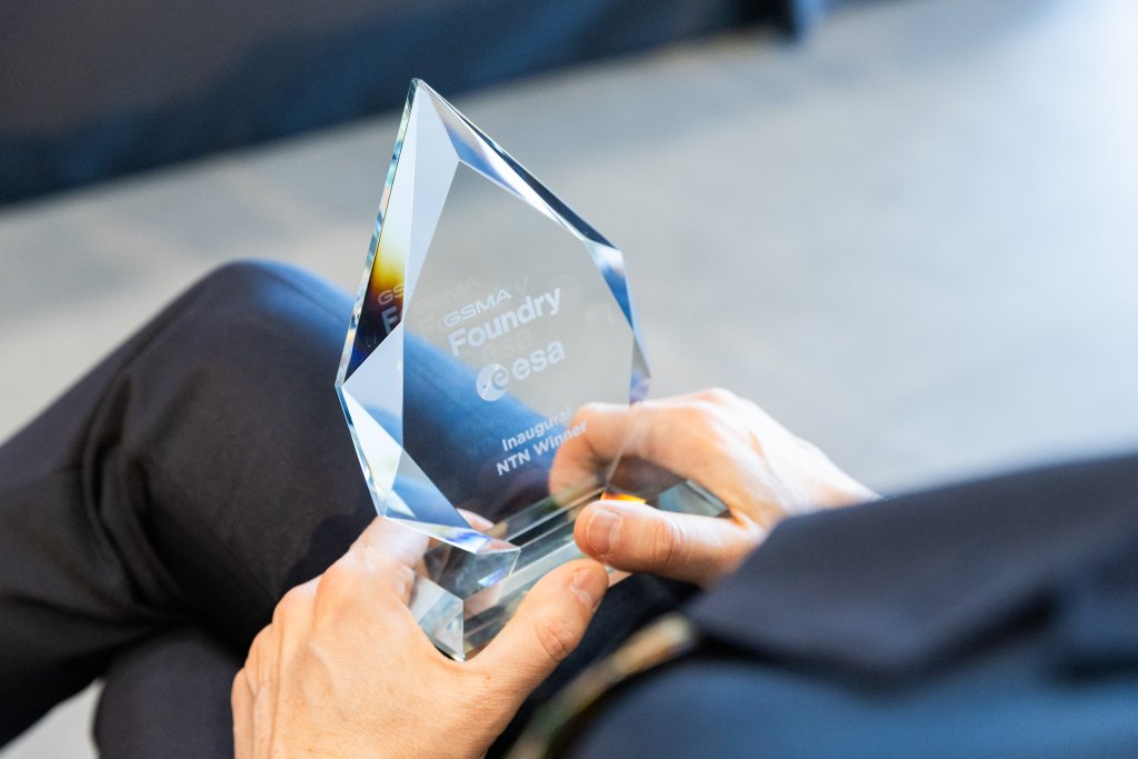 A person holds a crystal award engraved with "GSMA Foundry @esa Inaugural NTN Winner.