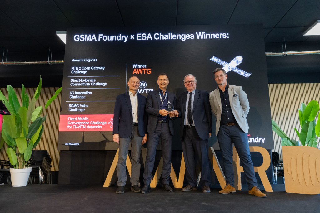 Four men stand on stage smiling, holding an award, in front of a screen announcing ESA Challenge winners.