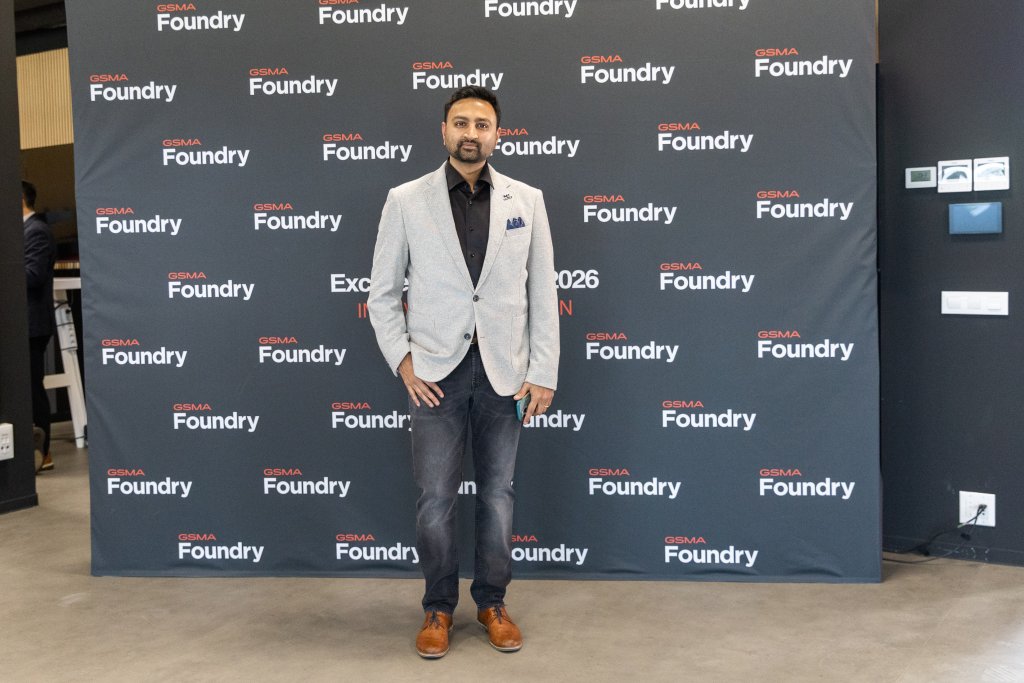 Man in a light gray blazer and jeans poses in front of a GSMA Foundry step-and-repeat banner.