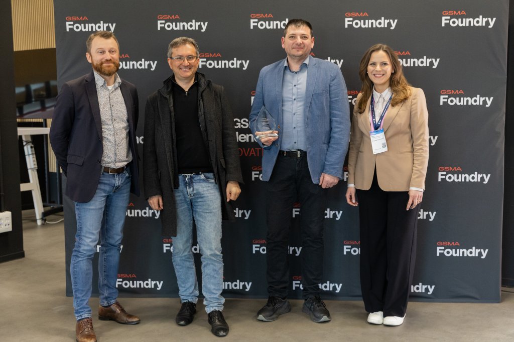 Four people stand in front of a GSMA Foundry backdrop, one holding a glass award, smiling at the camera.