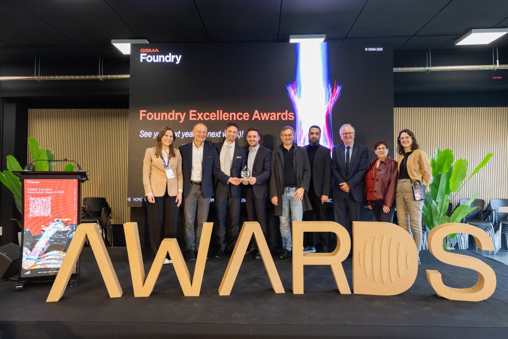 A group of people stand on stage smiling with an "AWARDS" sign and a Foundry Excellence Awards display behind them.