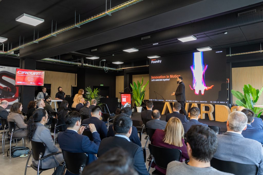 A speaker presents "Innovation in Motion" to an audience at a business conference in a modern venue.