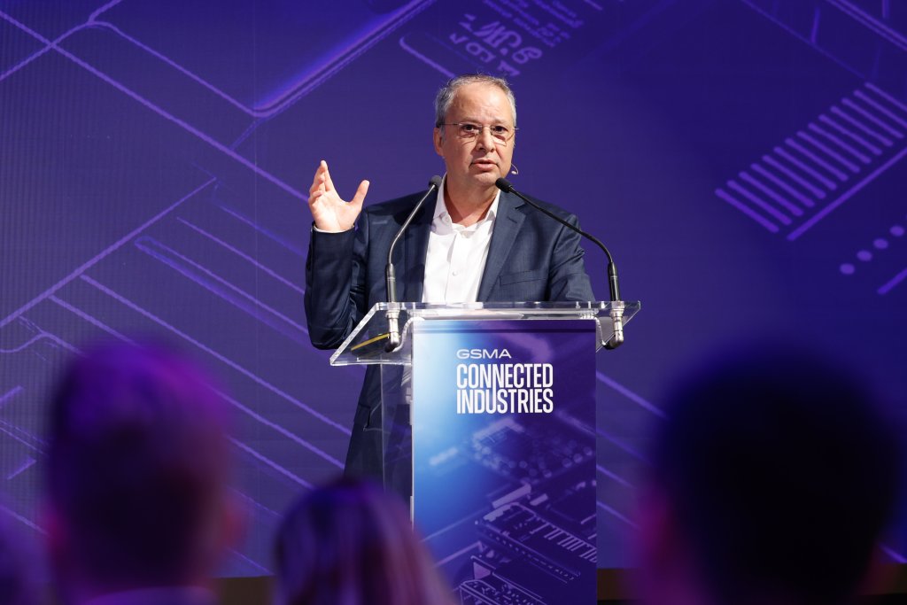 A man in a suit speaks at a podium labeled "GSMA Connected Industries" on a purple-lit stage.