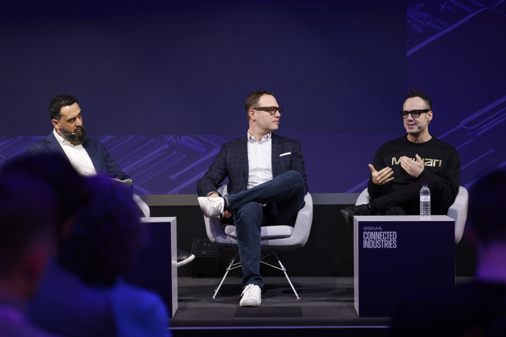 Three men sit on stage in a panel discussion at a technology conference, speaking and listening attentively.