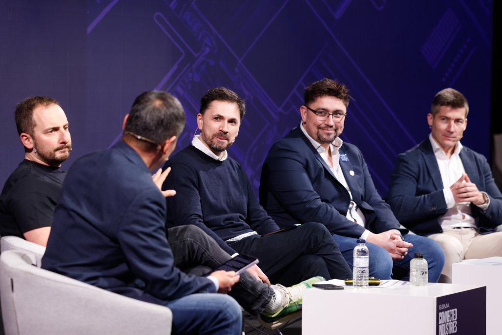 Five men in business attire sit on a panel, engaged in discussion at a conference.