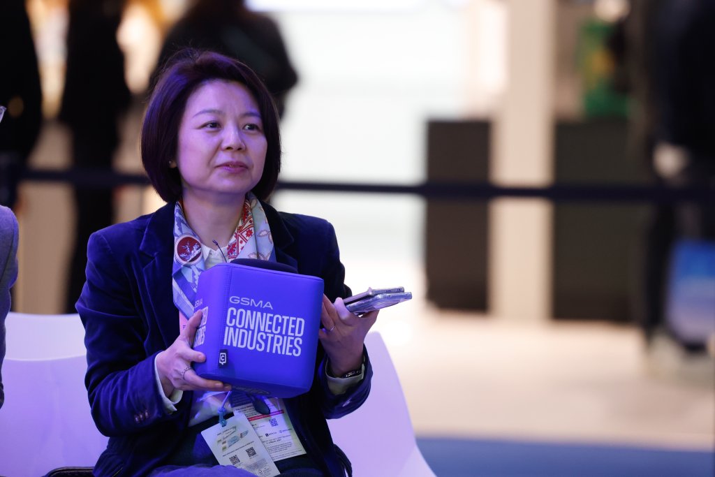 A woman holding a blue "GSMA Connected Industries" pouch and a phone at an event.
