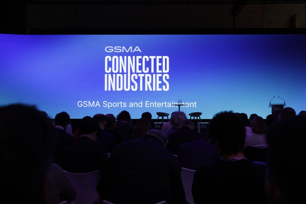 Audience facing a large screen displaying "GSMA Connected Industries" at an event, with chairs and podium on stage.