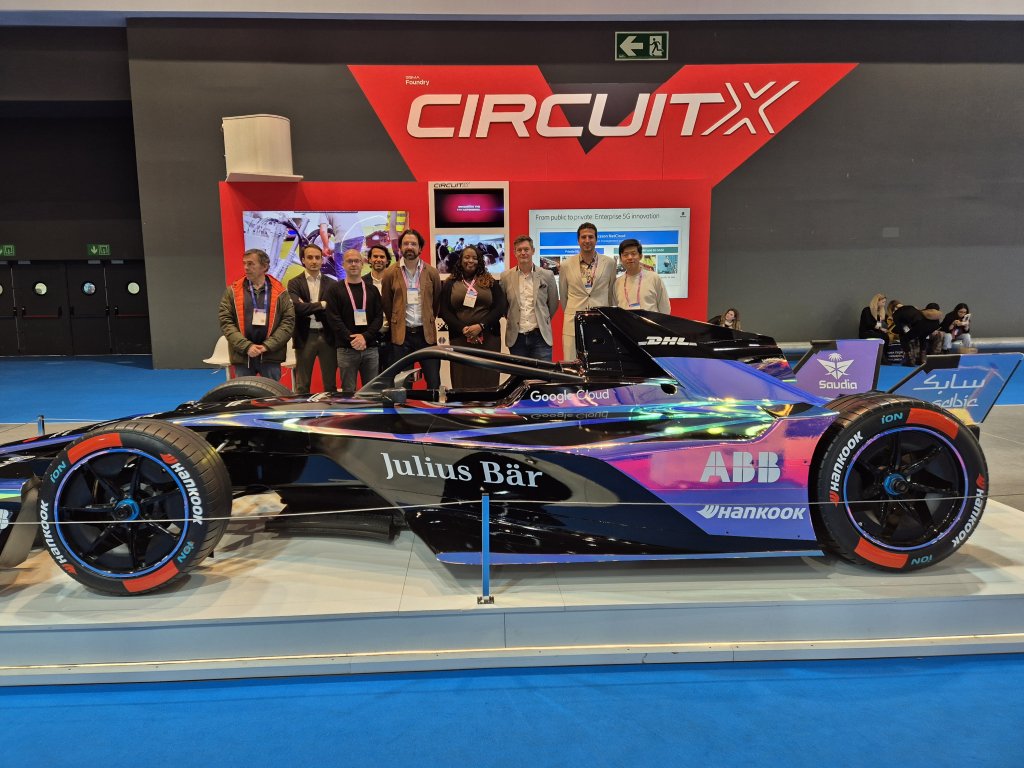 A group of people stands behind a black and purple Formula E race car at an indoor event.
