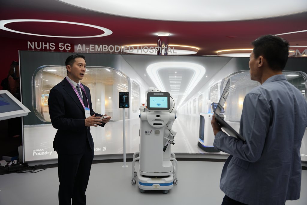 Two men talk near a medical robot in a modern exhibit labeled "NUHS 5G AI-EMBEDDED HOSPITAL.
