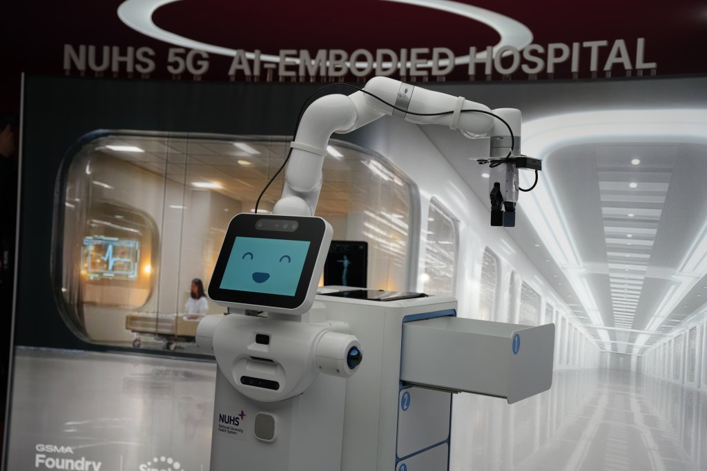 A friendly-faced robot stands in a futuristic hospital corridor under a sign reading "NUHS 5G AI-EMBODIED HOSPITAL.