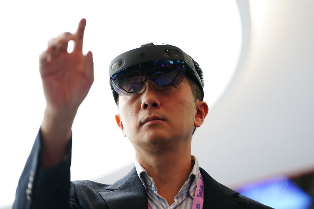 A man wearing augmented reality glasses interacts with a virtual display using his raised hand.