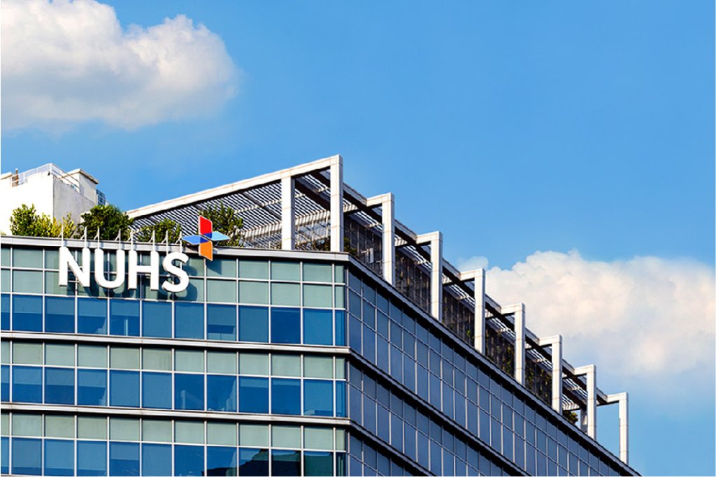 Glass building with "NUHS" sign and rooftop greenery under a blue sky with clouds, showcasing innovation in partnership with GSMA Foundry Partners.