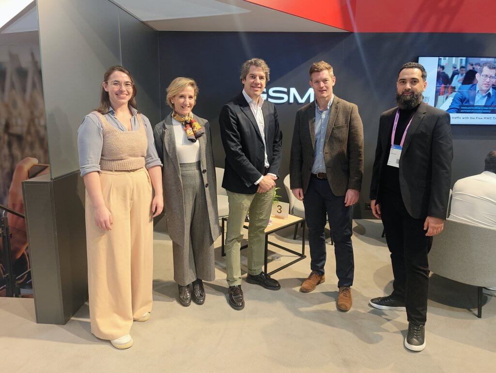 Five people stand and pose for a group photo in a modern office or conference setting.
